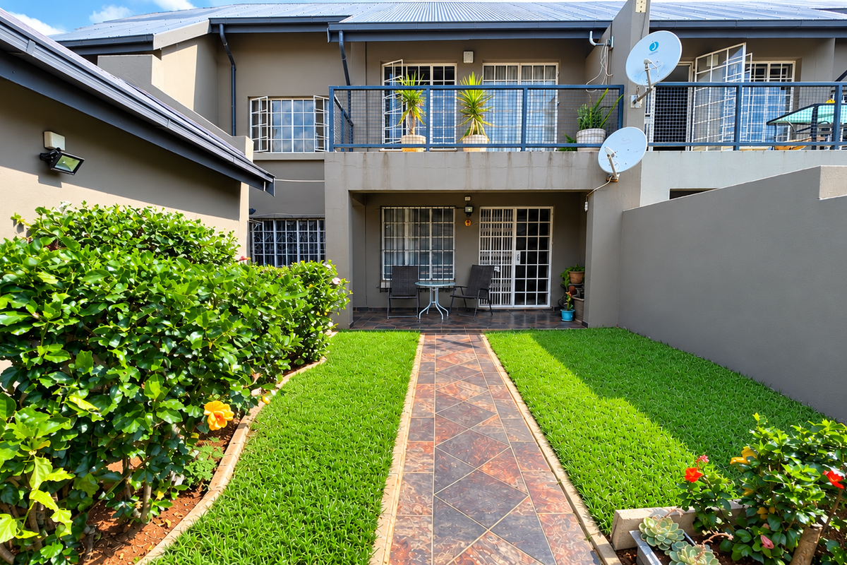 Rear view of a townhouse featuring a private garden, paved walkway, covered patio, and an upper-level balcony with security features.