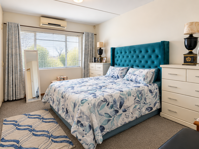 A well-maintained bedroom featuring built-in cupboards, carpeted flooring, and a wall-mounted air conditioning unit, offering a comfortable and functional living space.