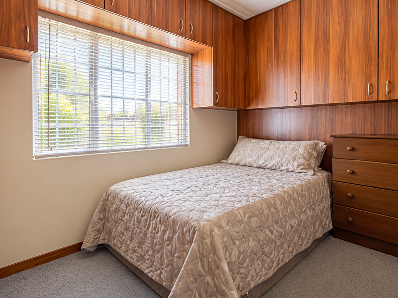 A bedroom featuring extensive built-in wooden cabinetry, overhead storage, and a matching headboard panel, providing ample storage space and a classic aesthetic.