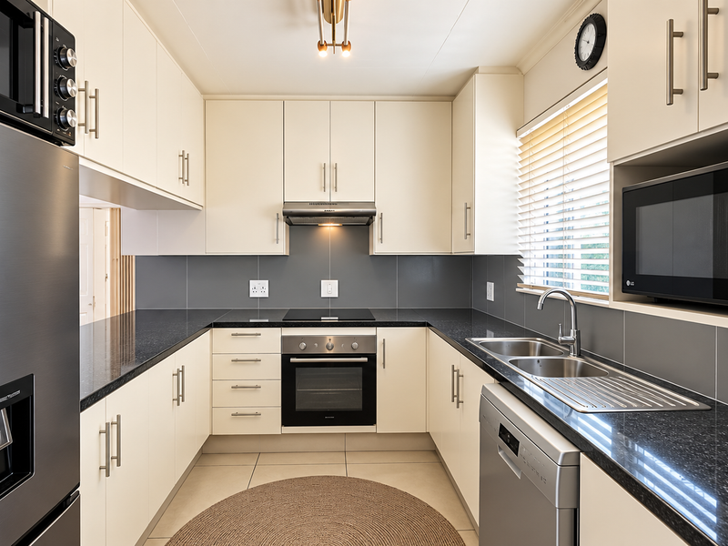 Modern U-shaped kitchen featuring sleek cream cabinetry, dark granite countertops, integrated appliances, and a tiled backsplash for a clean, functional workspace.