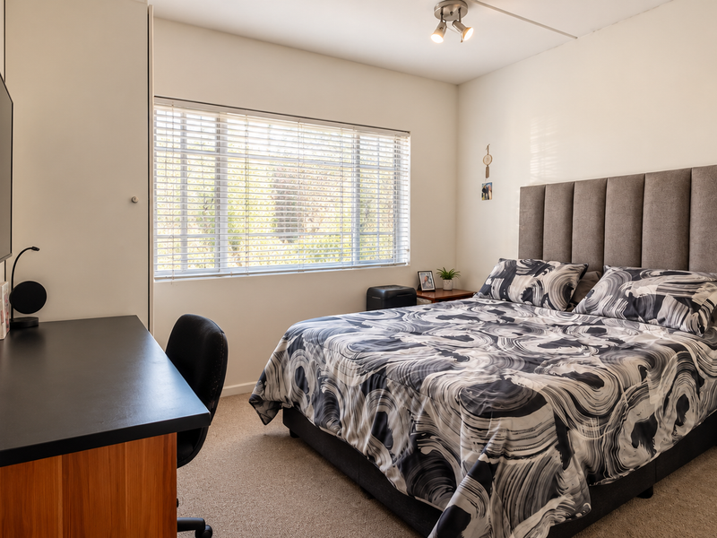 A well-maintained bedroom featuring neutral walls, carpet flooring, a built-in wardrobe, and venetian blinds allowing natural light.
