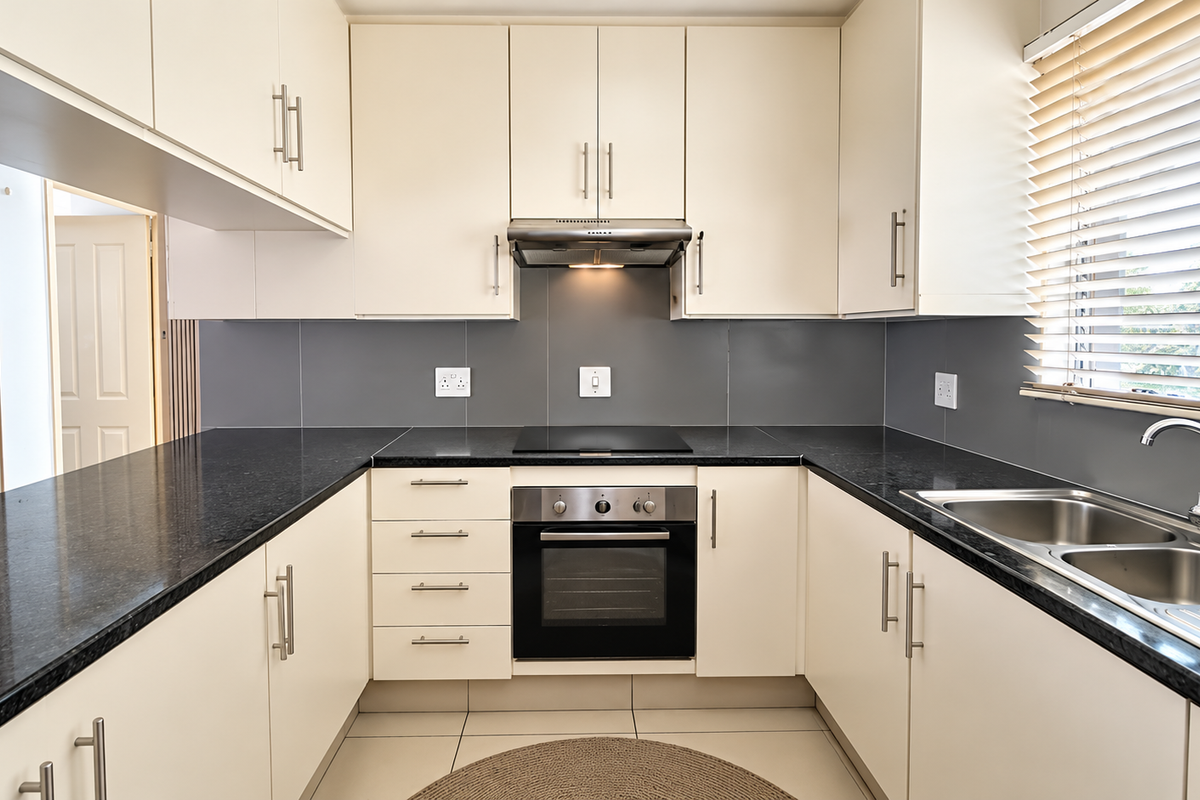A clean, modern kitchen featuring cream cabinetry, dark granite countertops, stainless steel appliances, and a functional U-shaped layout with ample storage.