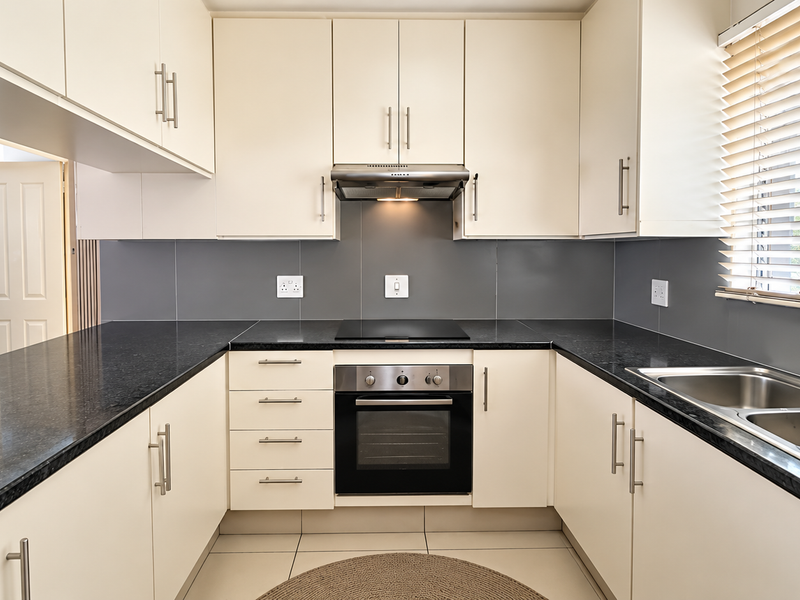 A clean, modern kitchen featuring cream cabinetry, dark granite countertops, stainless steel appliances, and a functional U-shaped layout with ample storage.