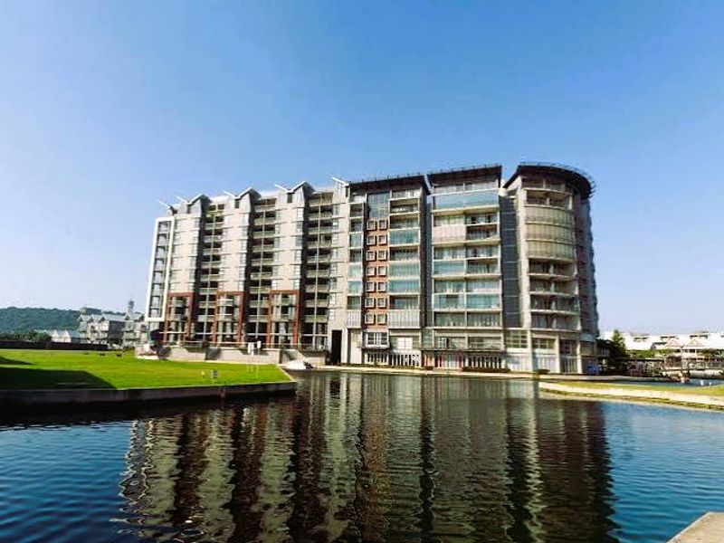 A view of a modern multi-story apartment complex situated directly on a waterfront, featuring numerous balconies and large glass windows.