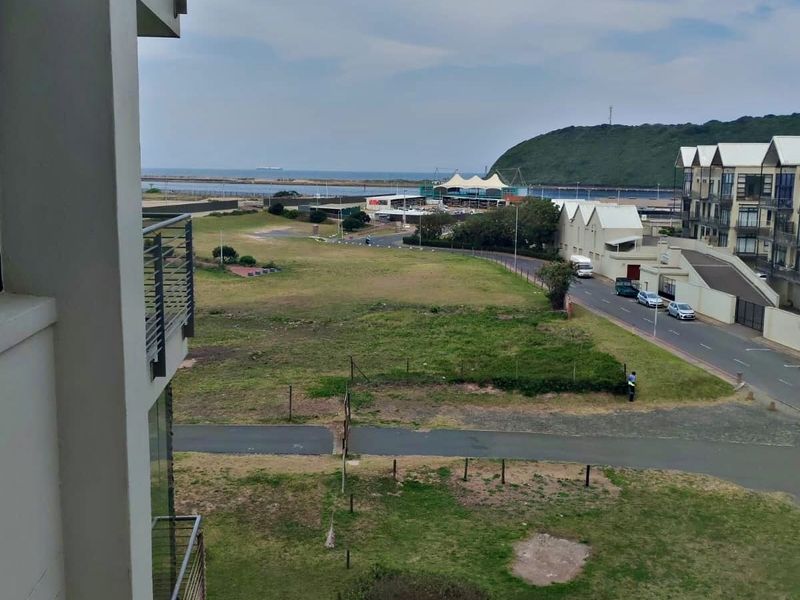Elevated view overlooking the surrounding neighborhood, green space, and distant coastal landscape from the apartment balcony.