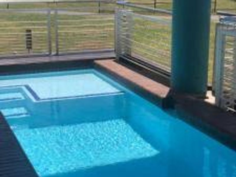 A private swimming pool featuring timber decking and a modern metal balustrade, overlooking an open green space.