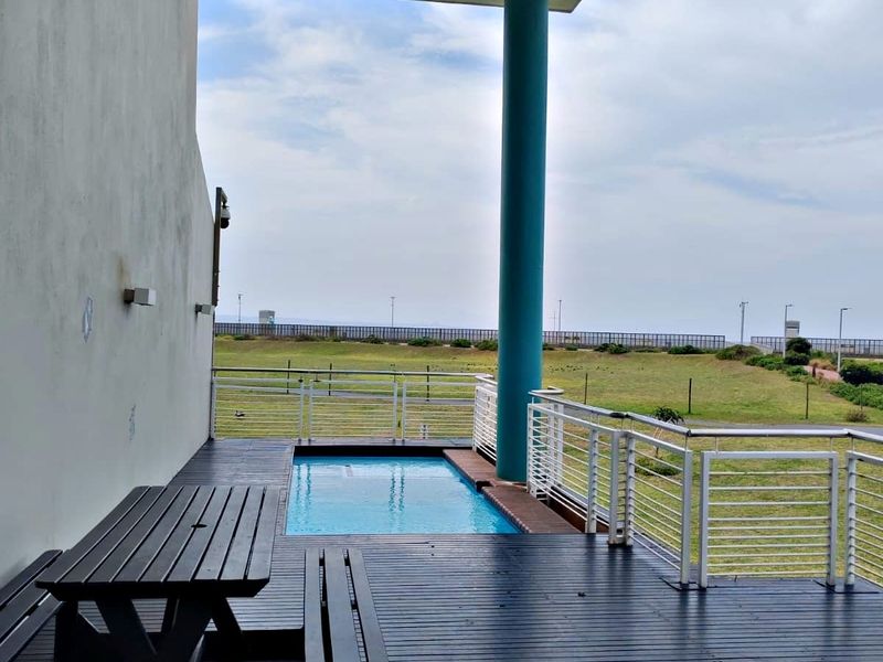 A covered outdoor deck featuring a built-in plunge pool, timber flooring, and metal balustrades overlooking an open landscape.