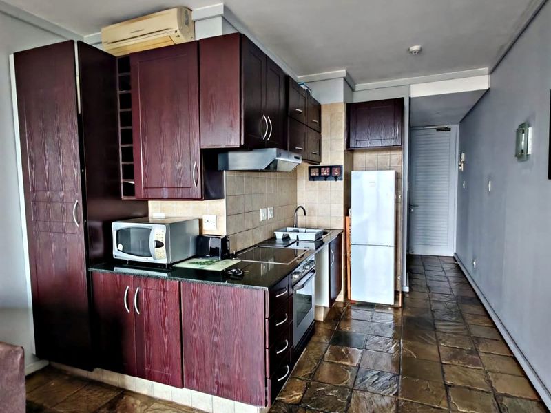 Compact kitchen featuring dark wood cabinetry, granite countertops, built-in oven, hob, and extractor fan, finished with stone-style floor tiles.