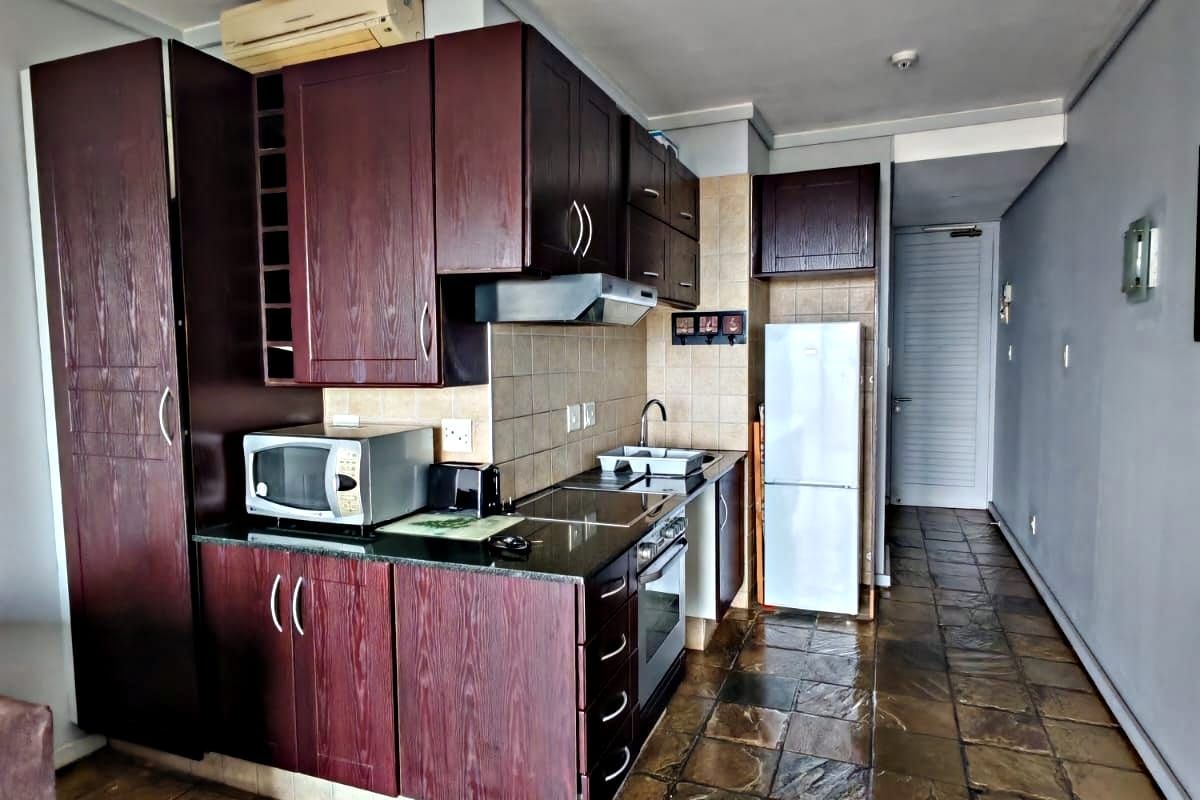 Compact kitchen featuring dark wood cabinetry, granite countertops, built-in oven, hob, and extractor fan, finished with stone-style floor tiles.