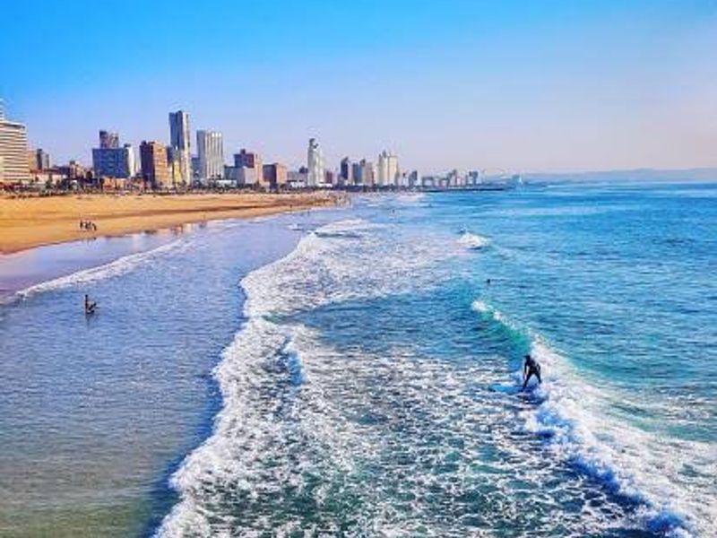 A scenic coastal view overlooking the ocean, sandy beach, and city skyline in the distance.