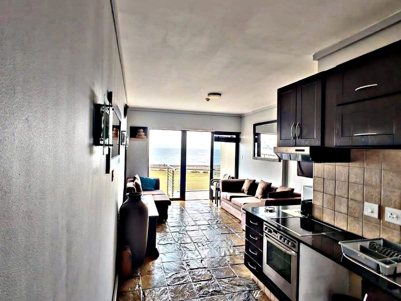 Open-plan living area featuring a kitchen with dark cabinetry, stone flooring, and sliding doors leading to a balcony with ocean views.