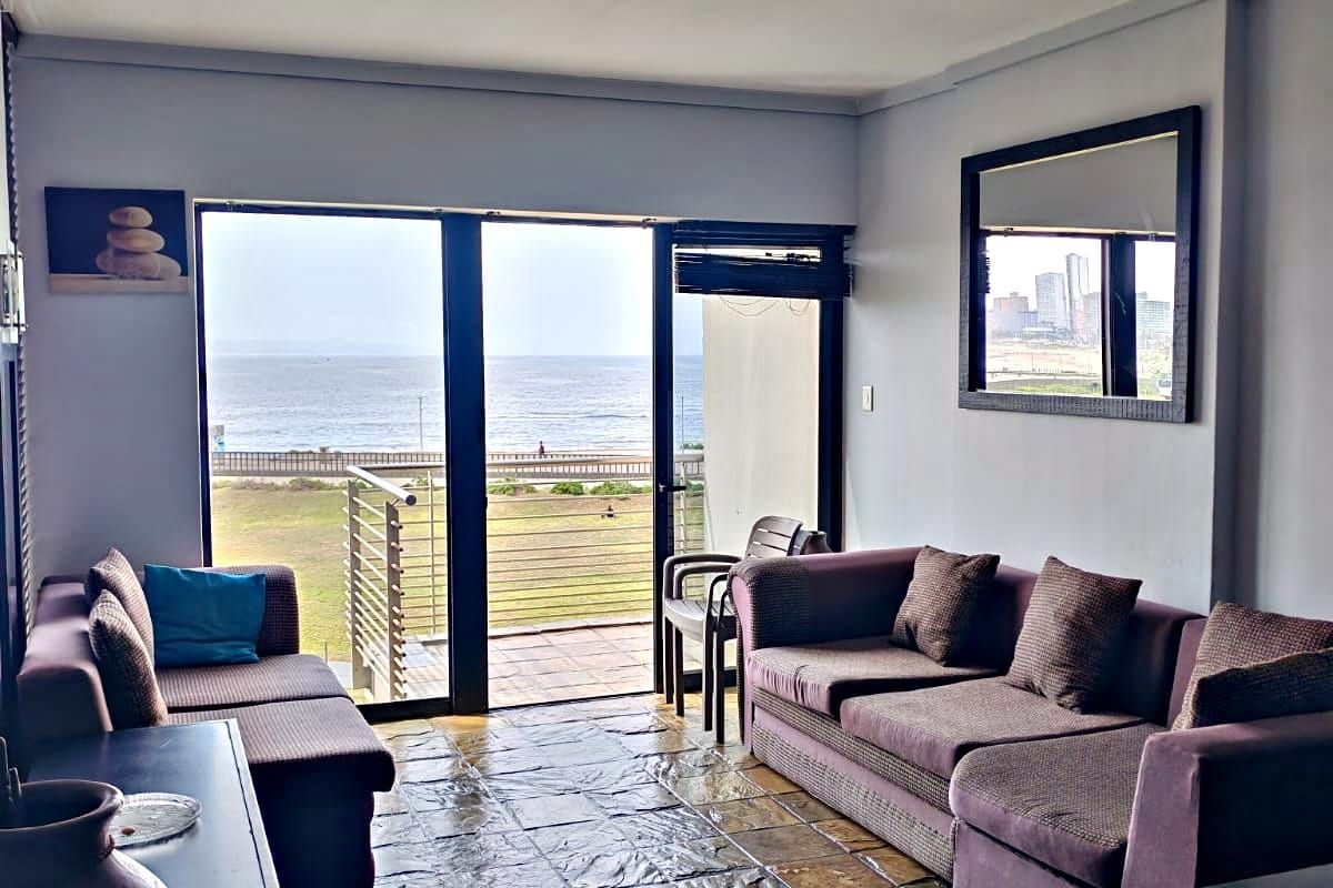 Living room featuring stone tile flooring and large sliding glass doors that open onto a balcony with ocean views.