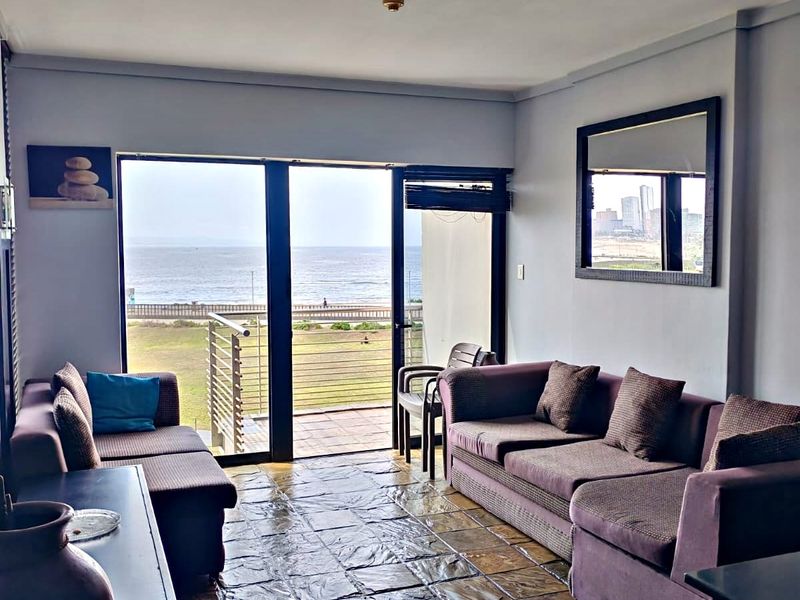 Living room featuring stone tile flooring and large sliding glass doors that open onto a balcony with ocean views.