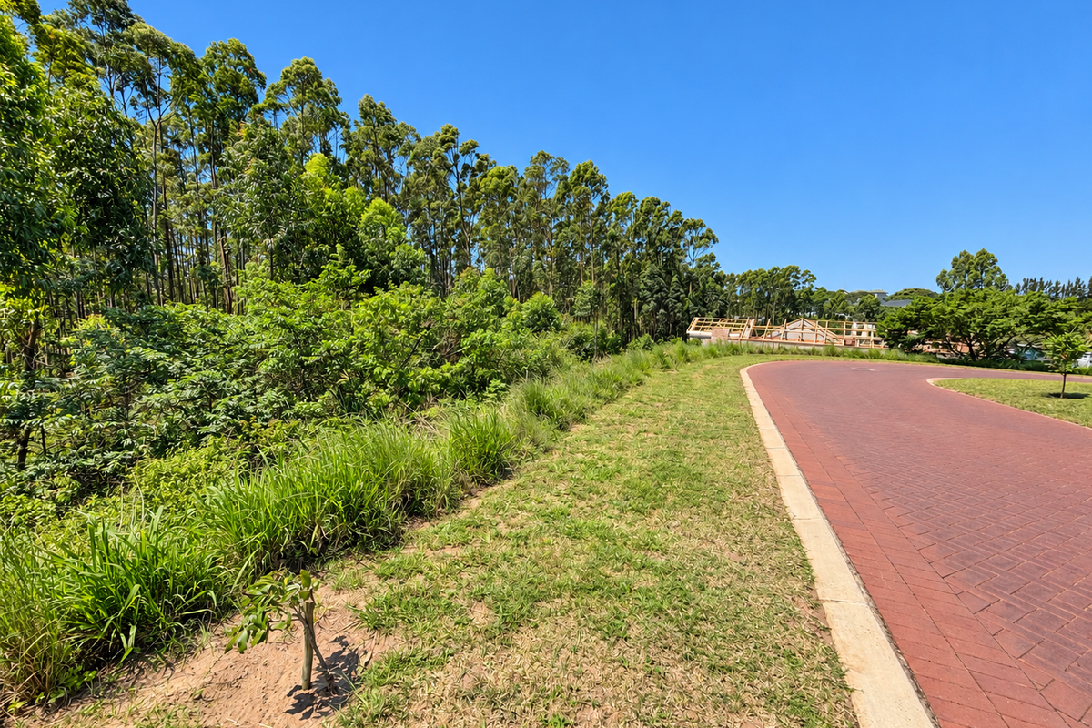 A view of a paved residential street with concrete curbing, adjacent to a landscaped verge and mature trees.