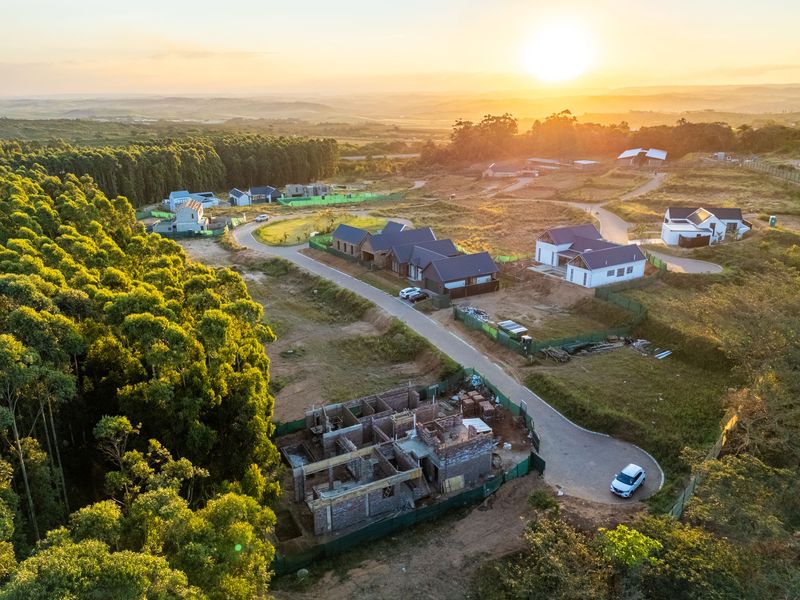 Aerial view of a residential development estate featuring multiple homes in various stages of construction, surrounded by natural landscape and paved access roads.