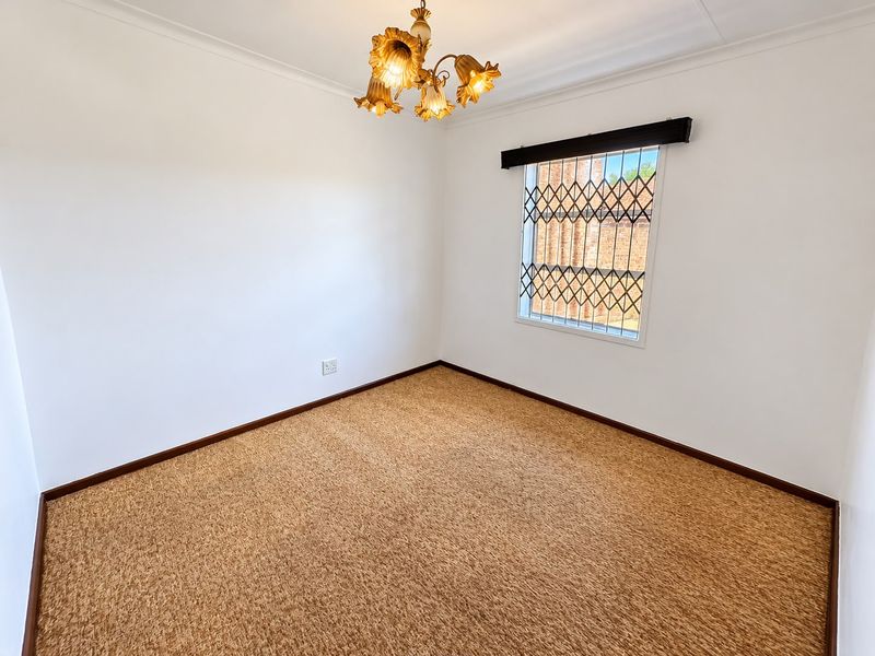 A clean, empty bedroom featuring neutral walls, carpeted flooring, and a window fitted with a security gate.