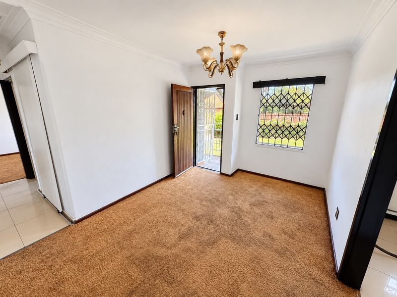 An empty living room featuring carpet flooring, a security gate at the entrance, and security bars on the window.