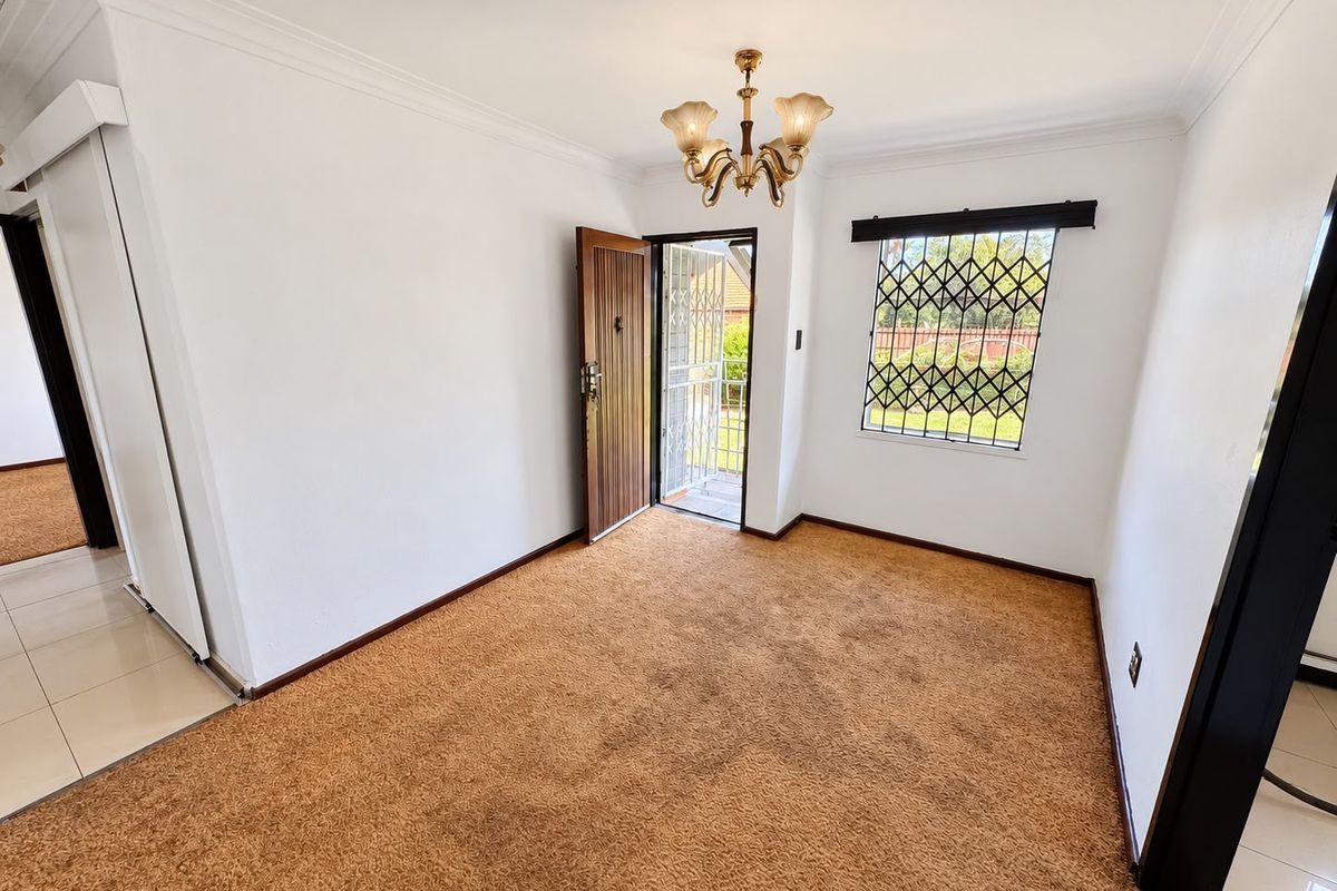 An empty living room featuring carpet flooring, a security gate at the entrance, and security bars on the window.