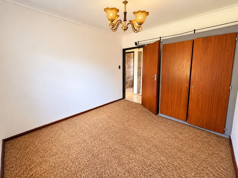 An empty bedroom featuring built-in wooden cupboards, carpeted flooring, and a classic chandelier light fixture.