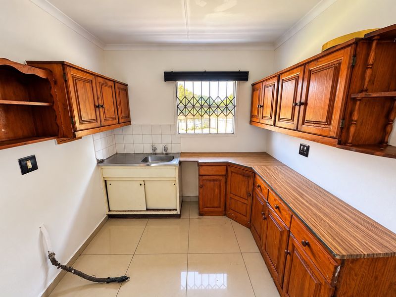 A functional kitchen featuring wooden cabinetry, laminate countertops, and tiled flooring, offering a blank canvas for potential modern updates and renovation.