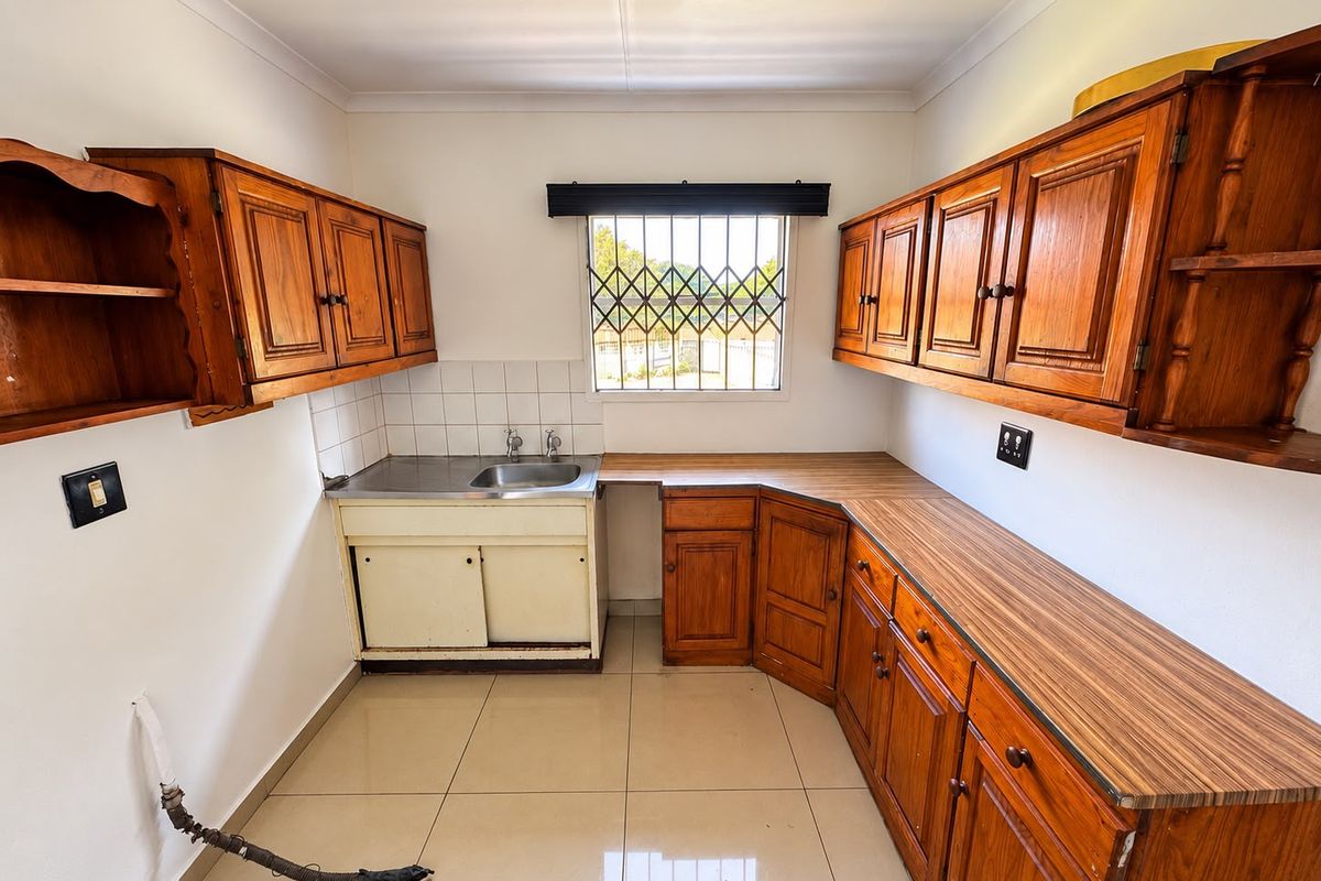 A functional kitchen featuring wooden cabinetry, laminate countertops, and tiled flooring, offering a blank canvas for potential modern updates and renovation.