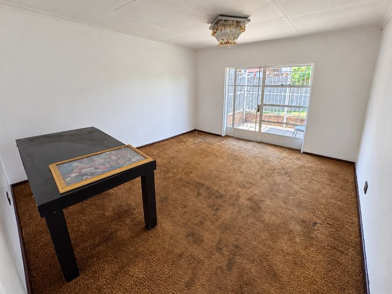 An empty living room featuring dated brown carpeting, a ceiling light fixture, and a sliding glass door with a security gate leading to the exterior.