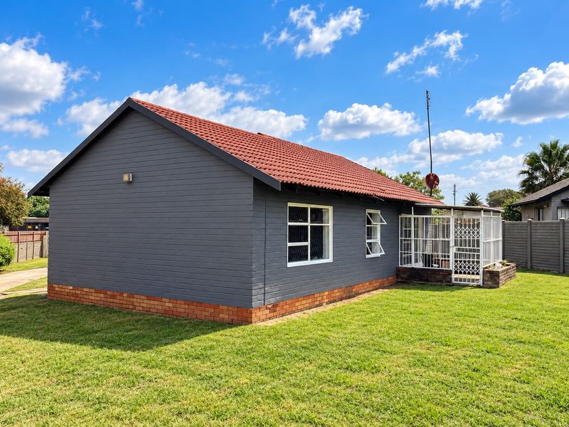 Rear view of the house featuring dark grey horizontal cladding, a red tiled roof, brick base, and an enclosed security-gated patio area.