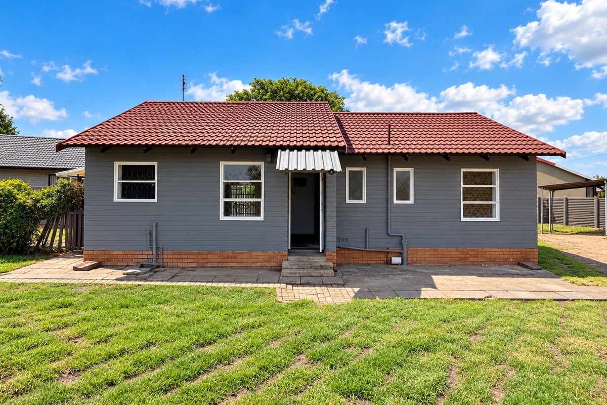 Rear view of a detached house featuring grey siding, a red tiled roof, and a paved patio area leading to the garden.