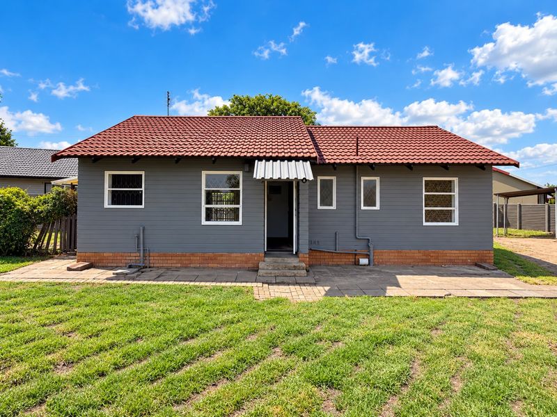 Rear view of a detached house featuring grey siding, a red tiled roof, and a paved patio area leading to the garden.