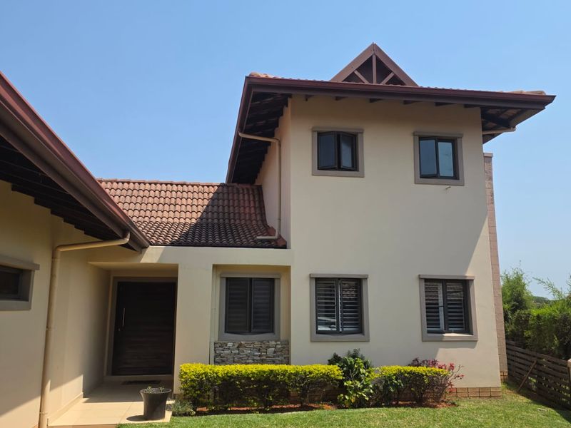 A well-maintained double-storey townhouse exterior featuring a tiled roof, stone cladding accents, paved entrance walkway, and a neat front lawn.