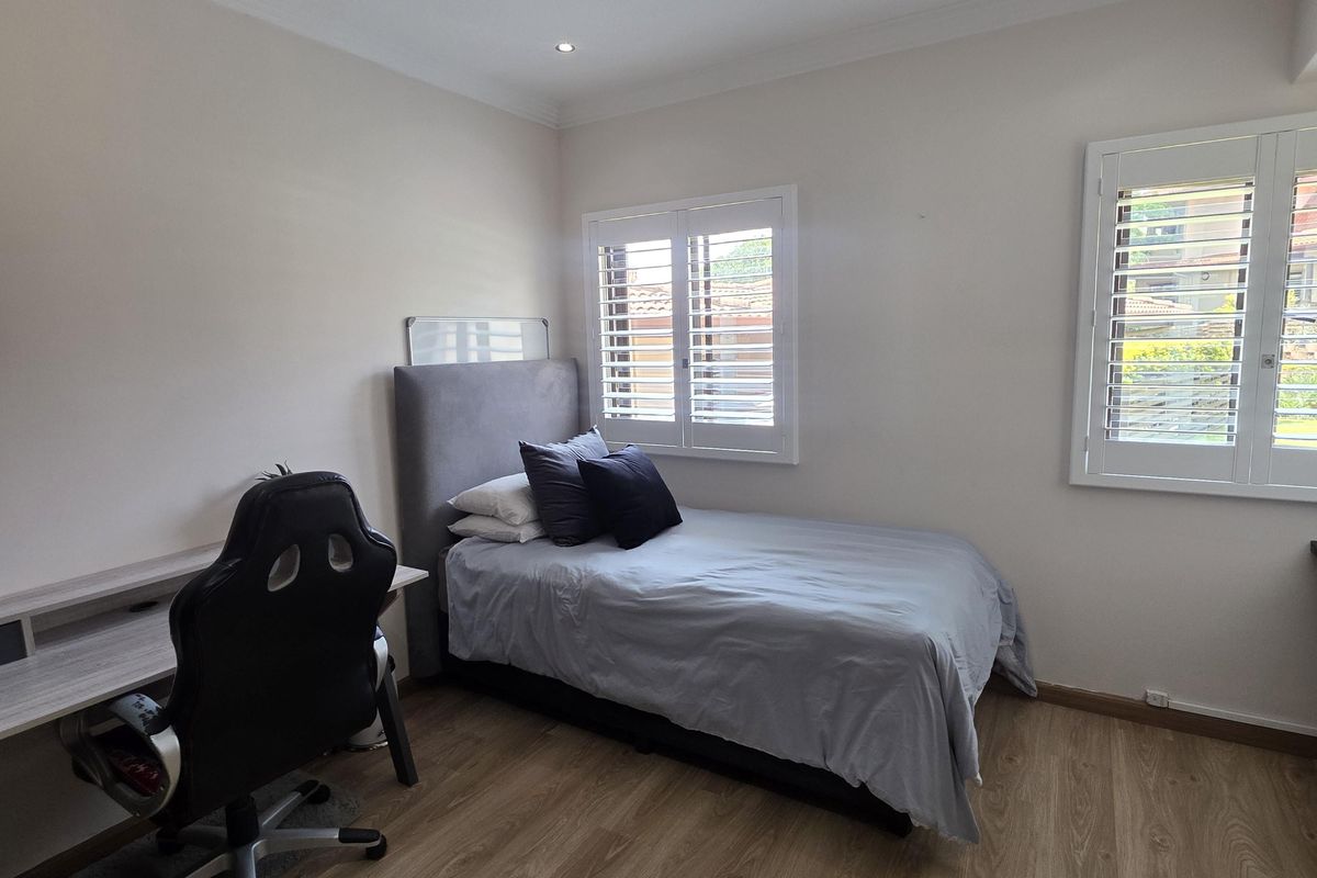 A well-maintained bedroom featuring light wood-look laminate flooring, plantation shutters, and recessed downlighting, offering a clean and neutral living space.