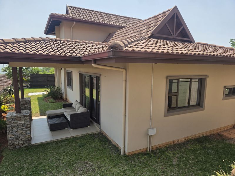 Rear view of the townhouse featuring a covered tiled patio, stone-clad support pillar, and well-maintained exterior walls with aluminium window frames.