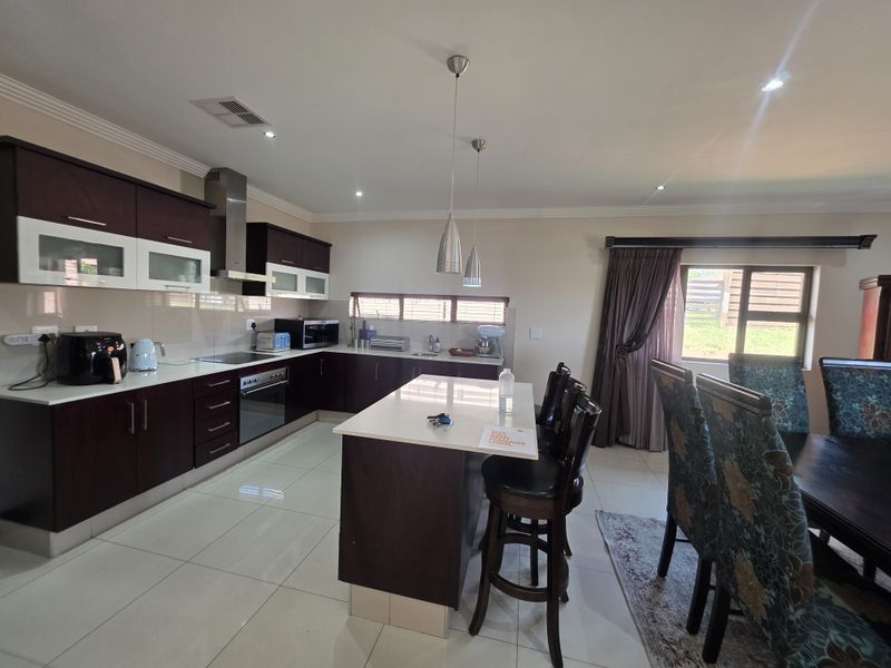 Spacious open-plan kitchen and dining area featuring dark wood cabinetry, stone countertops, a central island, and modern recessed lighting.