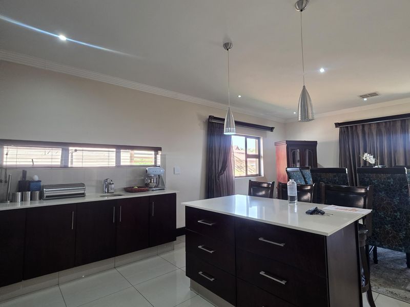 Spacious open-plan kitchen and dining area featuring a central island with stone countertops, dark cabinetry, modern pendant lighting, and polished tiled flooring.