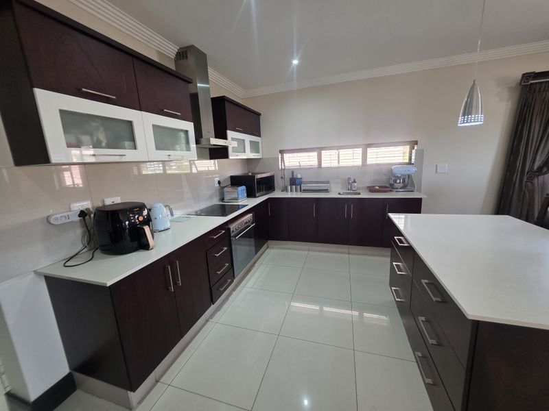 Modern kitchen featuring dark wood cabinetry, white stone countertops, a central island, and high-quality tiled flooring with integrated stainless steel appliances.