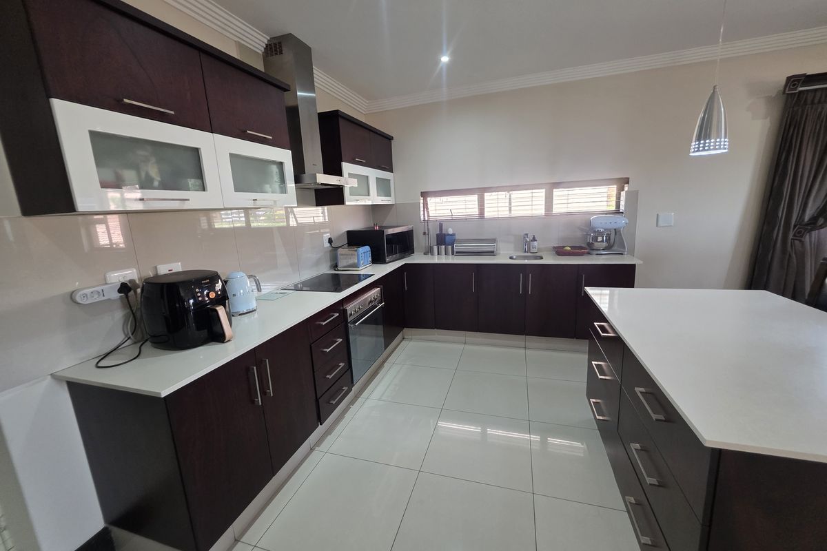Modern kitchen featuring dark wood cabinetry, white stone countertops, a central island, and high-quality tiled flooring with integrated stainless steel appliances.