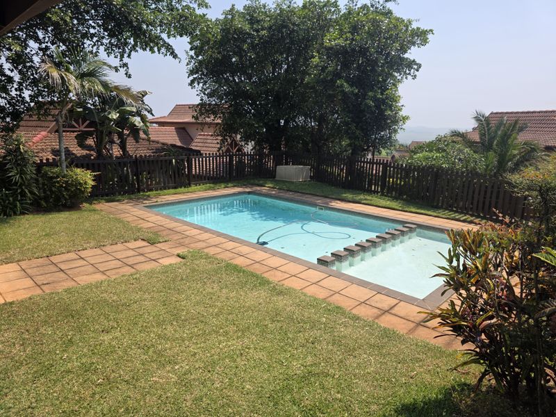 A private outdoor swimming pool area featuring a paved surround, established garden, and timber perimeter fencing within a residential townhouse setting.