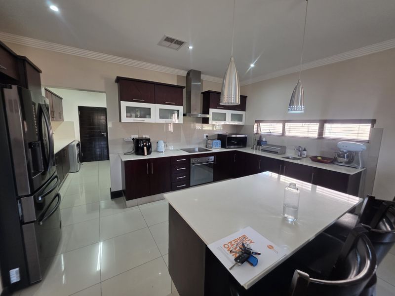 Modern kitchen featuring dark wood cabinetry, stone countertops, a central island, and integrated stainless steel appliances, complemented by tiled flooring and contemporary lighting.