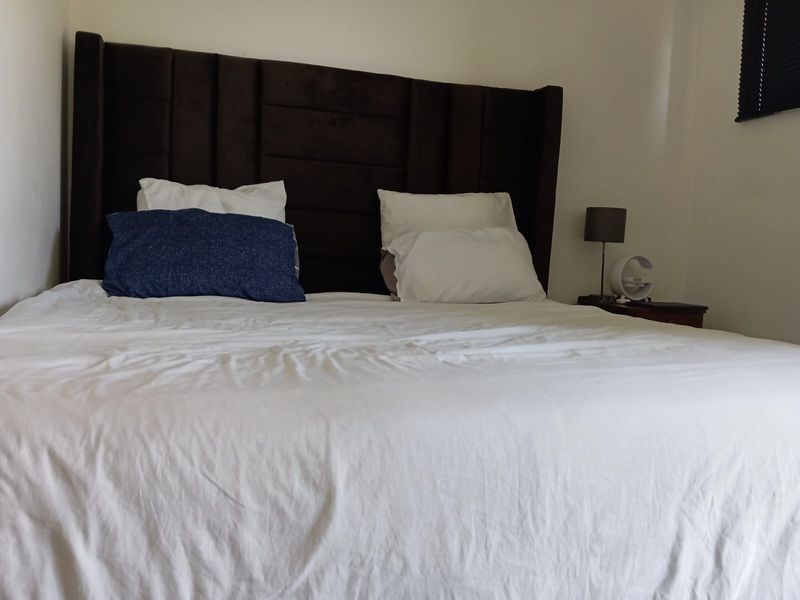A bedroom featuring a dark upholstered headboard and a window fitted with a black venetian blind.