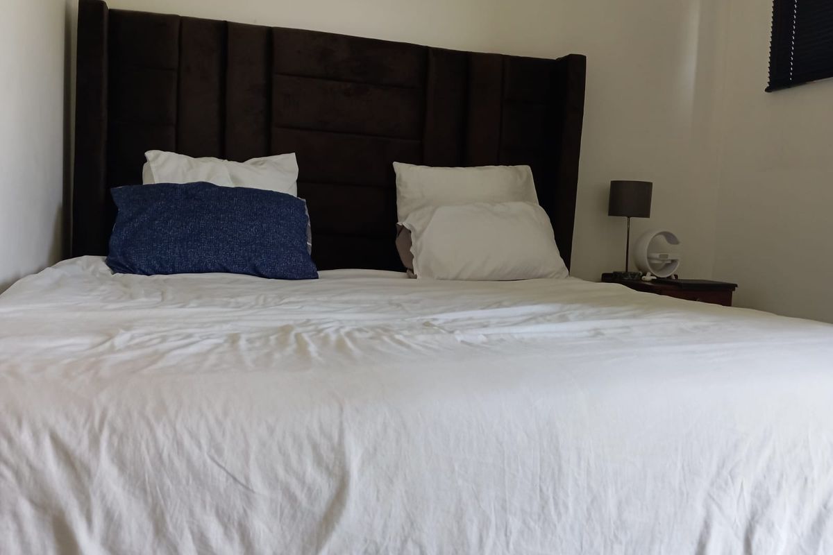 A bedroom featuring a dark upholstered headboard and a window fitted with a black venetian blind.