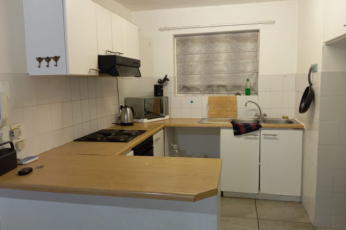 A functional kitchen featuring white cabinetry, laminate countertops, an electric hob, and a stainless steel double sink with tiled splashbacks.