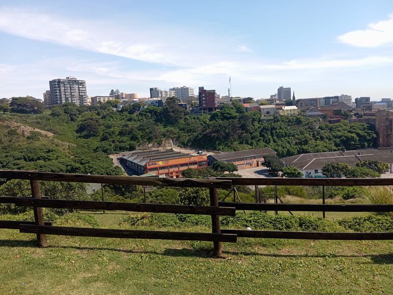 An elevated view overlooking a green valley and urban cityscape, framed by a timber fence in the foreground.
