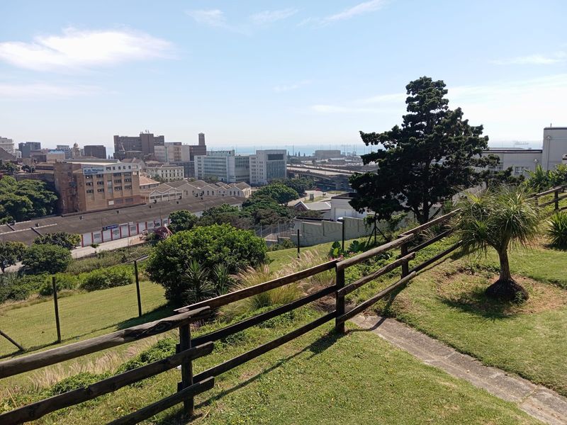 Elevated outdoor area featuring a timber fence and landscaped lawn, offering expansive views over the surrounding city and industrial landscape.