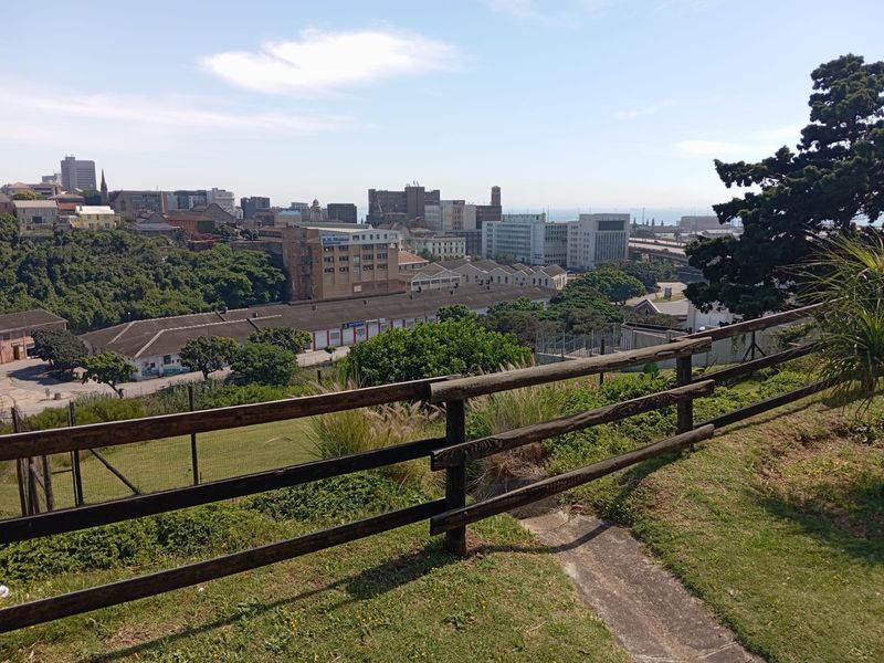 An elevated outdoor view overlooking the surrounding urban landscape and industrial buildings, framed by a timber post and rail fence.
