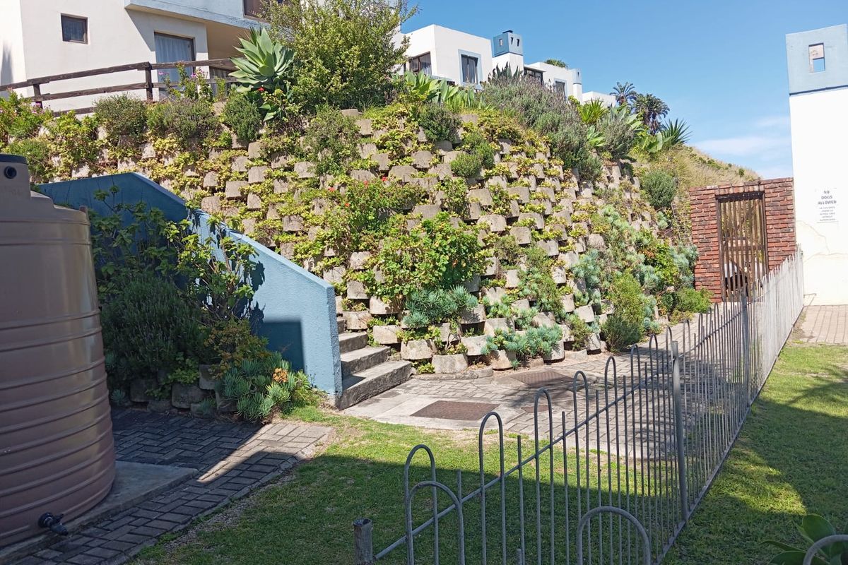 Exterior view of the apartment complex rear area featuring a landscaped retaining wall, concrete stairs, paved pathways, and a large water tank.