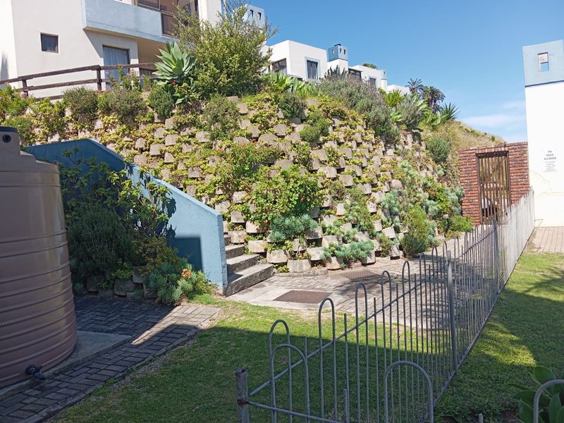 Exterior view of the apartment complex rear area featuring a landscaped retaining wall, concrete stairs, paved pathways, and a large water tank.