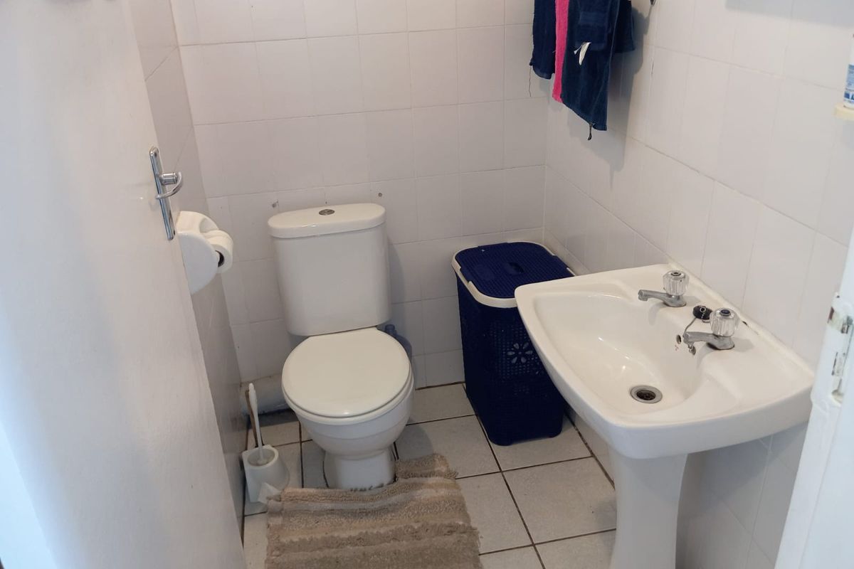 A compact bathroom featuring a pedestal washbasin and a standard toilet, finished with white ceramic wall and floor tiles.