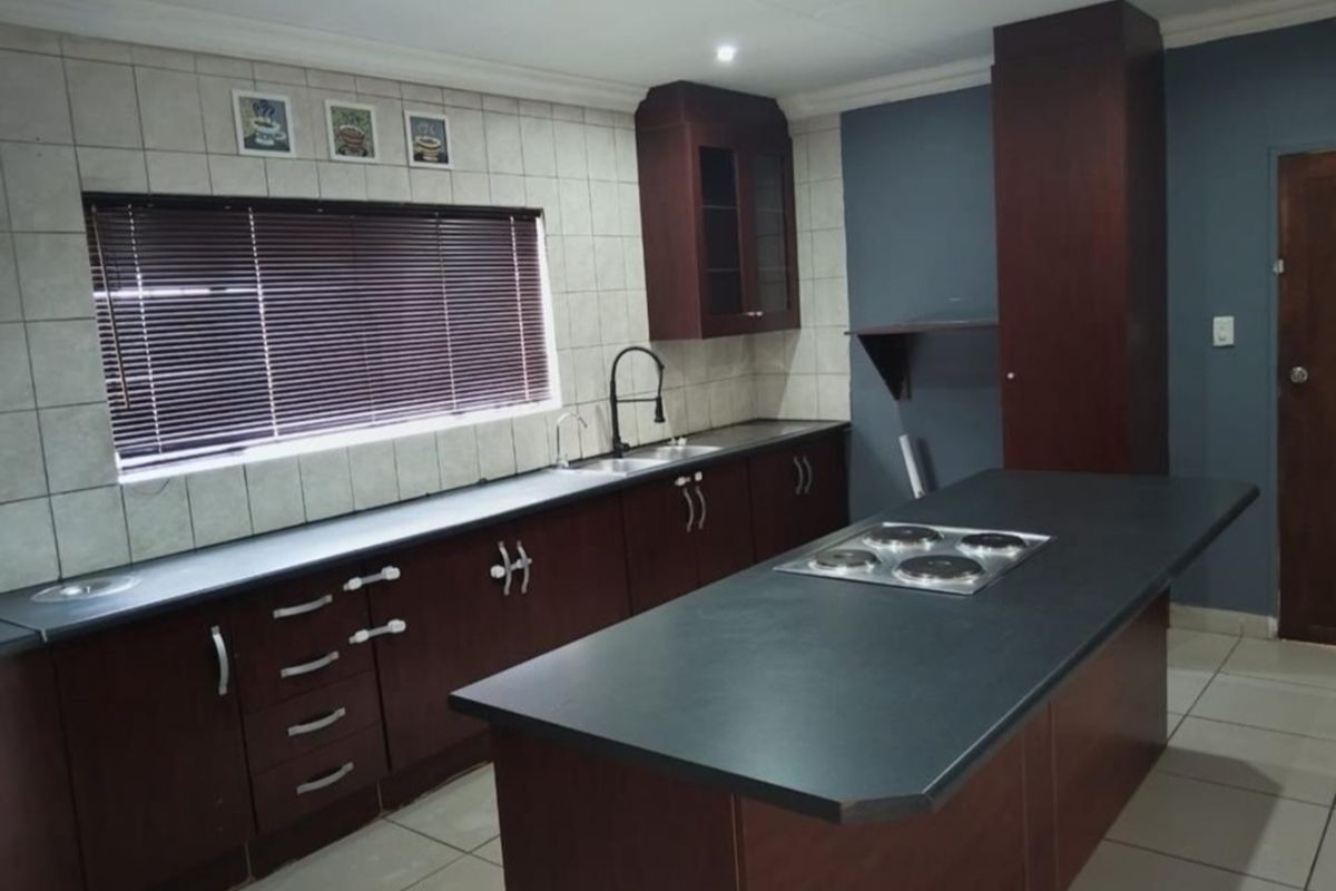 A functional kitchen featuring dark wood cabinetry, a central island with an integrated electric hob, tiled backsplash, and ample counter space.