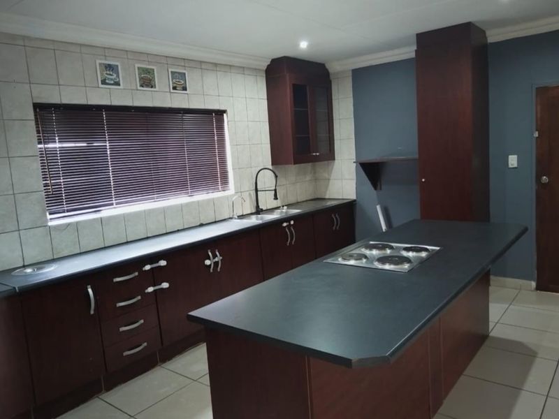A functional kitchen featuring dark wood cabinetry, a central island with an integrated electric hob, tiled backsplash, and ample counter space.