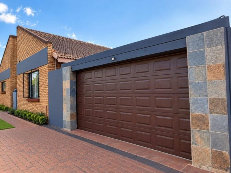 A well-maintained double garage featuring a modern sectional door, brick exterior, and decorative stone cladding, complemented by a neat paved driveway.